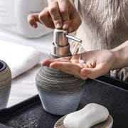 Person dispensing soap from a retro brushed ceramic bathroom wash set.